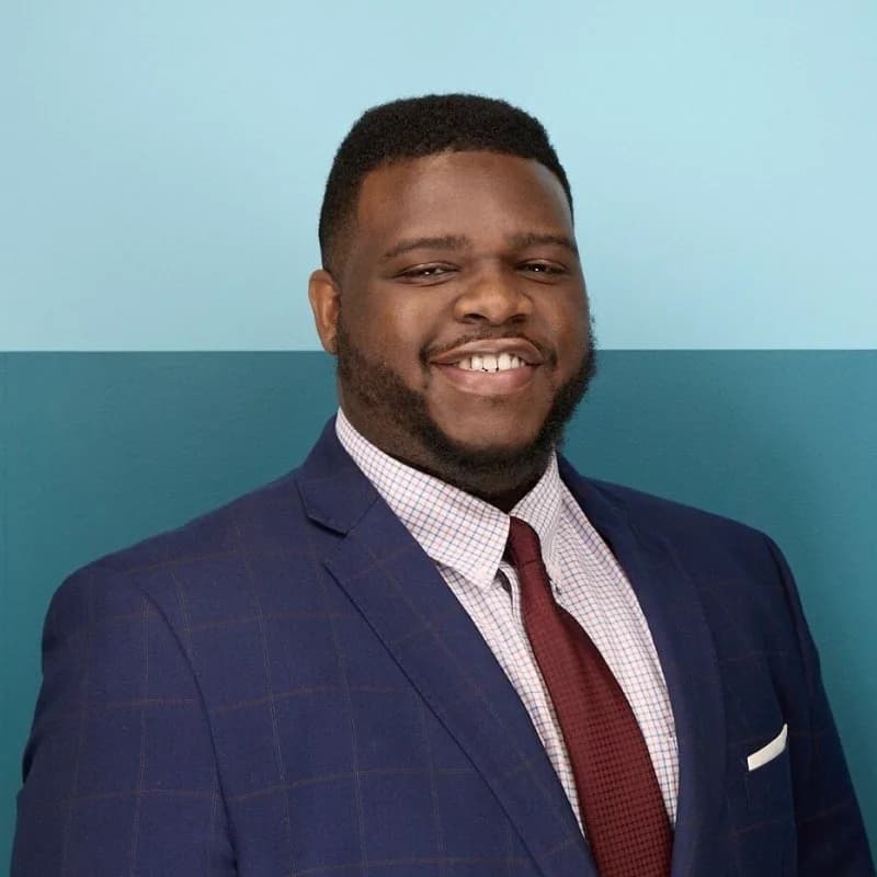 Tyrance Billingsley II, smiling in a navy windowpane suit and burgundy tie