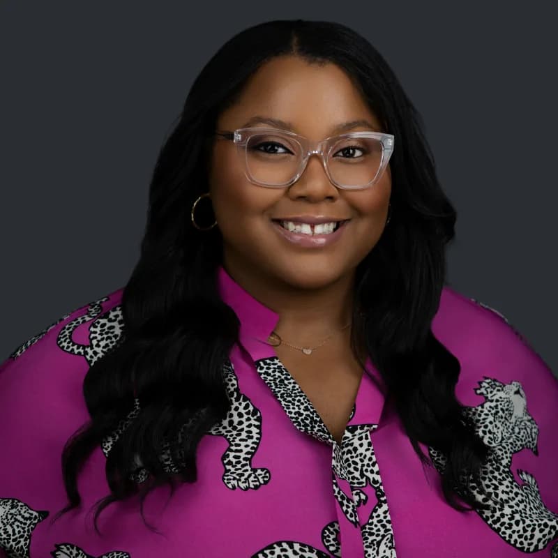 Symone Gittens, smiling in clear-framed glasses and a magenta patterned blouse